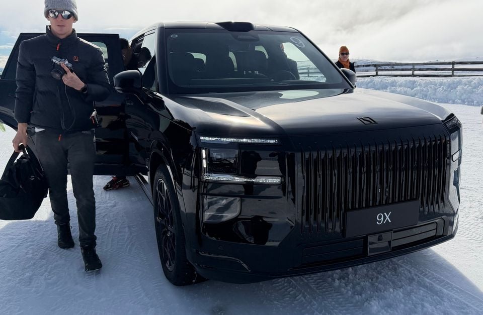 A black Zeekr 9X SUV parked in a snowy landscape, seen from the front, with a person standing beside the open driver's door holding a camera.