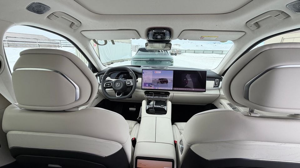 Interior view of a Zeekr SUV showing white leather seats, a large widescreen infotainment display, and a digital rear-view mirror, shot from the rear cabin looking forward